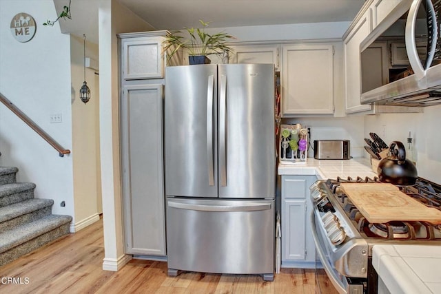 kitchen with light wood-type flooring, tile countertops, and appliances with stainless steel finishes