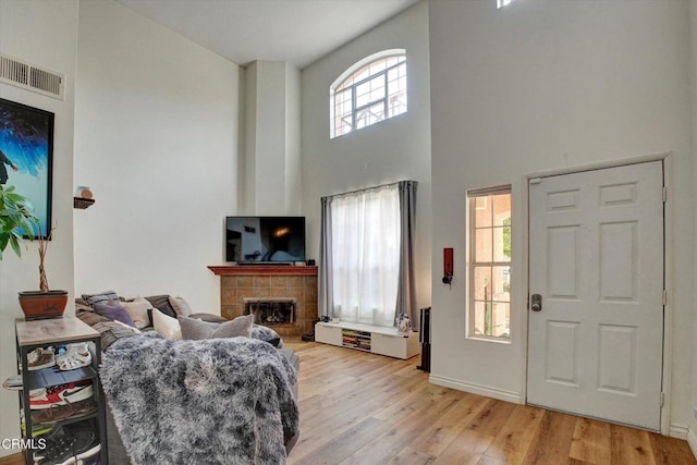 living room with a towering ceiling, a fireplace, and light hardwood / wood-style floors