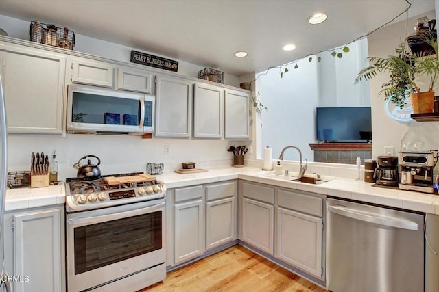 kitchen with stainless steel appliances, tile countertops, sink, and light wood-type flooring