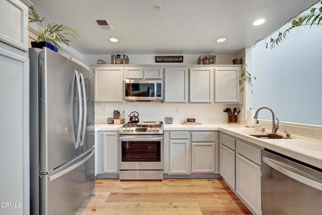 kitchen with white cabinets, appliances with stainless steel finishes, sink, and light wood-type flooring