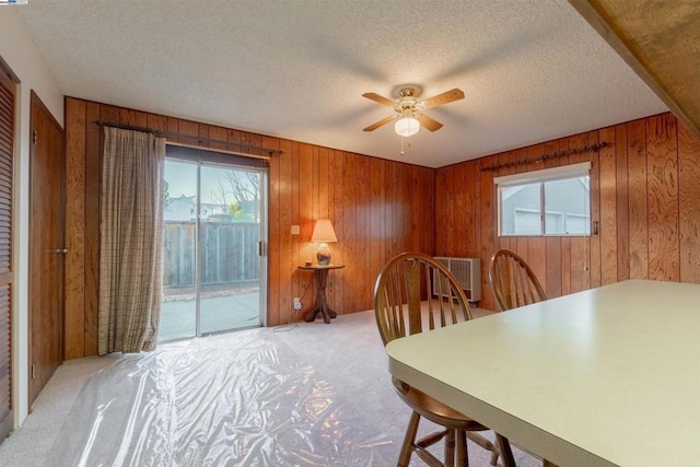 dining space with ceiling fan, wooden walls, light carpet, and a textured ceiling