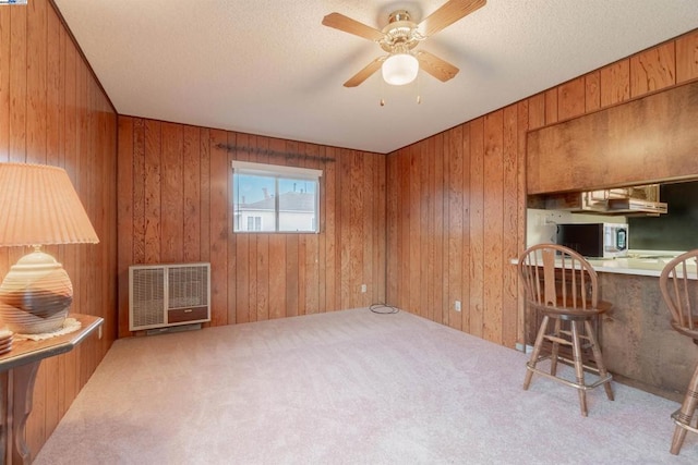 carpeted home office featuring heating unit, ceiling fan, and wood walls