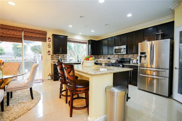 kitchen with a kitchen island, appliances with stainless steel finishes, plenty of natural light, ornamental molding, and light stone countertops