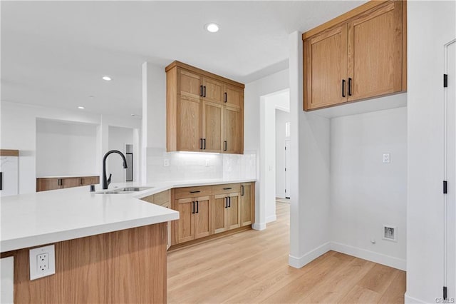 kitchen with tasteful backsplash, sink, light hardwood / wood-style flooring, and kitchen peninsula