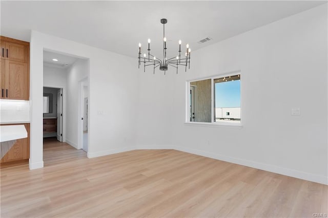 empty room featuring a chandelier and light hardwood / wood-style floors