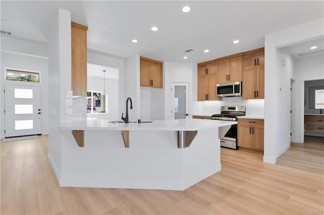 kitchen featuring a breakfast bar, sink, light wood-type flooring, kitchen peninsula, and stainless steel appliances