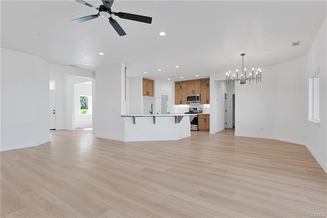 unfurnished living room with ceiling fan with notable chandelier and light wood-type flooring