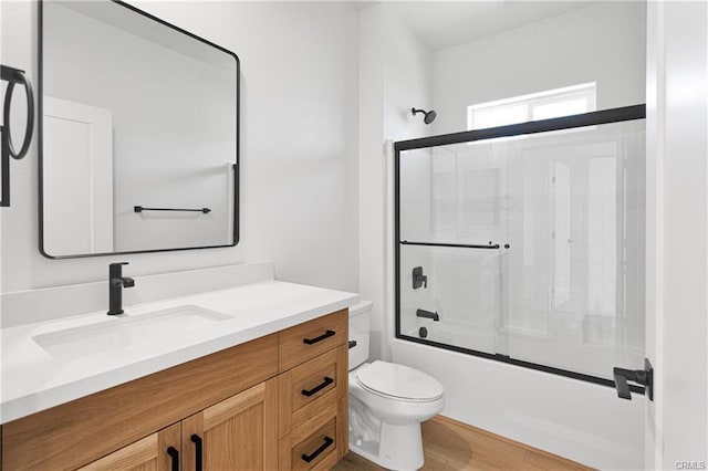 full bathroom featuring wood-type flooring, vanity, shower / bath combination with glass door, and toilet