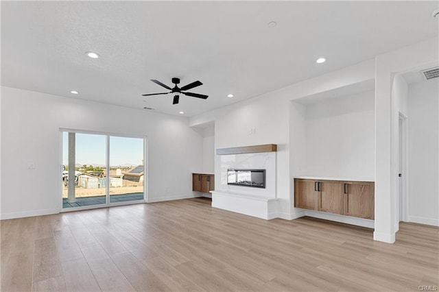 unfurnished living room featuring a multi sided fireplace, ceiling fan, and light hardwood / wood-style flooring