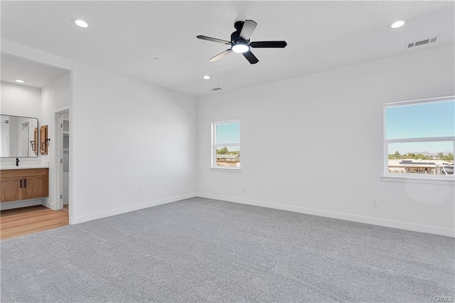 unfurnished bedroom featuring ceiling fan, light colored carpet, connected bathroom, and sink