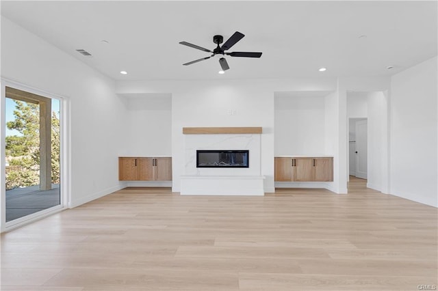 unfurnished living room featuring a high end fireplace, light hardwood / wood-style flooring, and ceiling fan