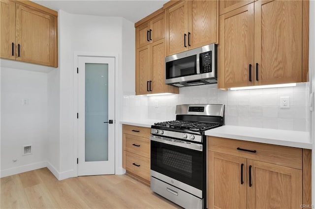 kitchen with stainless steel appliances, decorative backsplash, and light wood-type flooring