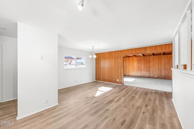 unfurnished living room featuring a notable chandelier, light hardwood / wood-style flooring, and wood walls