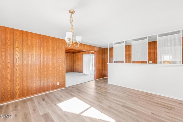 spare room featuring wood walls, a chandelier, and light hardwood / wood-style floors