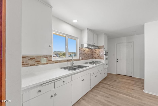 kitchen featuring sink, gas stovetop, white cabinetry, oven, and decorative backsplash