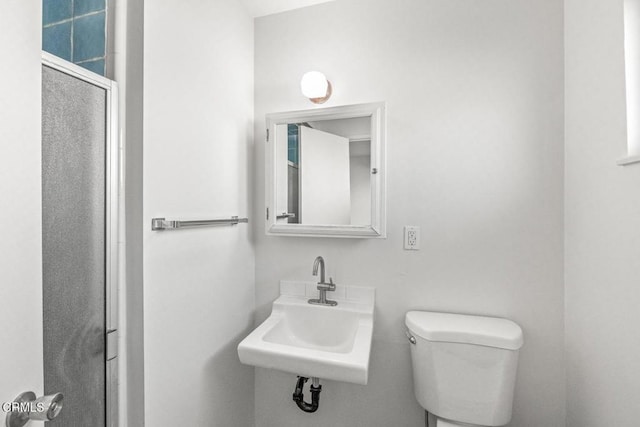 bathroom with sink, a shower with door, and toilet