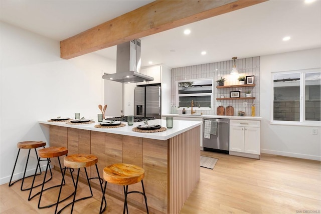 kitchen with a kitchen bar, island range hood, white cabinets, and appliances with stainless steel finishes