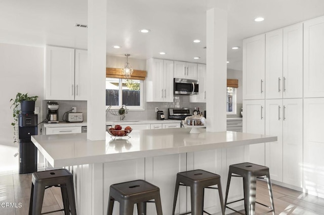 kitchen with appliances with stainless steel finishes, a breakfast bar area, white cabinets, and decorative backsplash