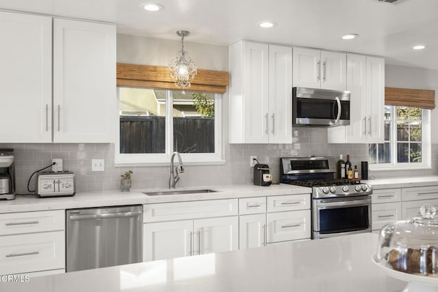 kitchen featuring sink, tasteful backsplash, appliances with stainless steel finishes, pendant lighting, and white cabinets