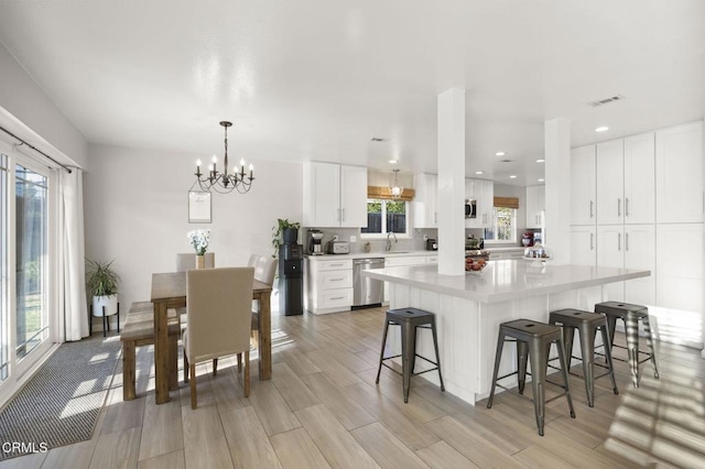 kitchen featuring a kitchen island, white cabinetry, sink, stainless steel dishwasher, and light hardwood / wood-style flooring