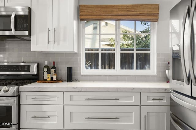 kitchen with white cabinetry, backsplash, light stone counters, and appliances with stainless steel finishes