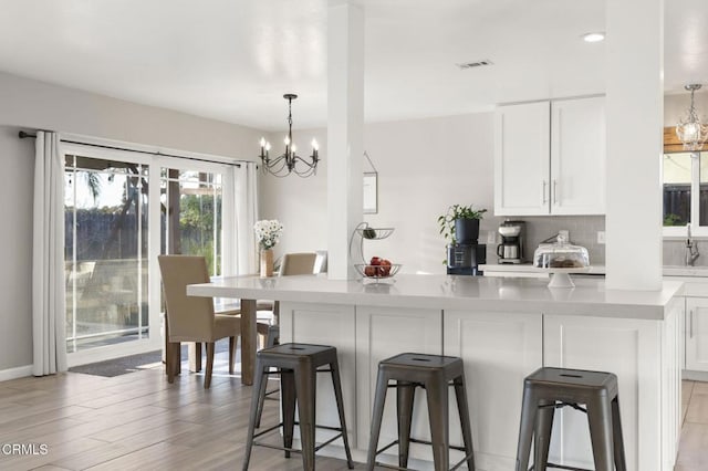 kitchen featuring a breakfast bar, white cabinetry, tasteful backsplash, light wood-type flooring, and pendant lighting