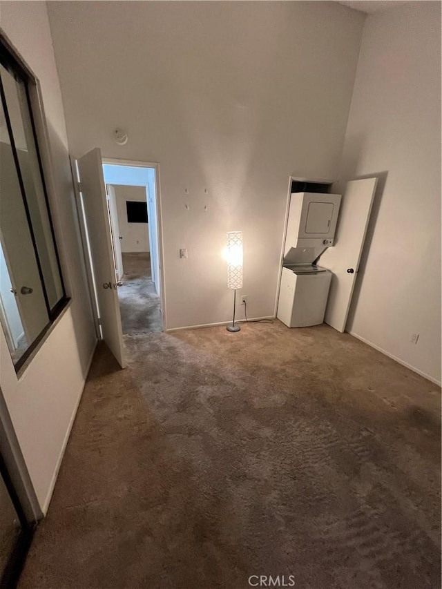 interior space featuring dark carpet, stacked washer and clothes dryer, and a high ceiling