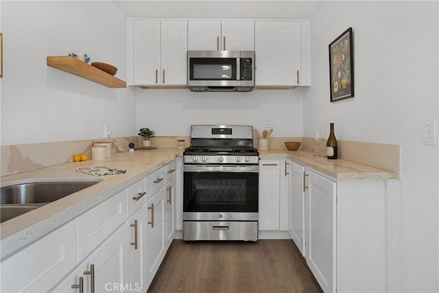 kitchen featuring appliances with stainless steel finishes, white cabinetry, sink, dark hardwood / wood-style flooring, and light stone counters