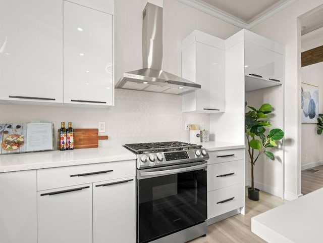 kitchen featuring white cabinets, wall chimney exhaust hood, crown molding, stainless steel range with gas stovetop, and light hardwood / wood-style flooring