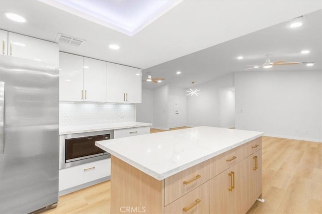 kitchen with white cabinetry, light hardwood / wood-style flooring, a kitchen island, stainless steel appliances, and decorative backsplash