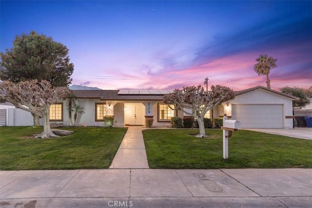 ranch-style home with a garage, a lawn, and solar panels