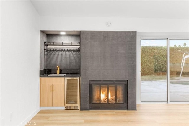 bar with light brown cabinetry, a large fireplace, sink, wine cooler, and light hardwood / wood-style floors