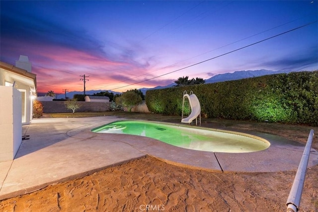 pool at dusk featuring a mountain view, a patio area, and a water slide