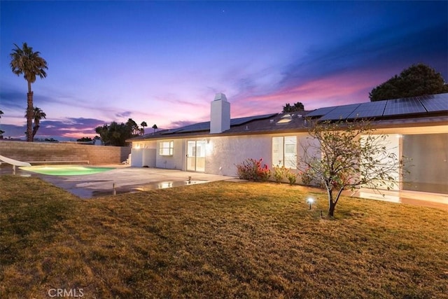 back house at dusk with a fenced in pool, a yard, a patio, and solar panels