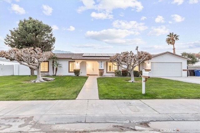 ranch-style home featuring a garage, a front lawn, and solar panels