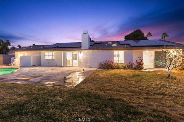 back house at dusk featuring a patio, a lawn, and solar panels