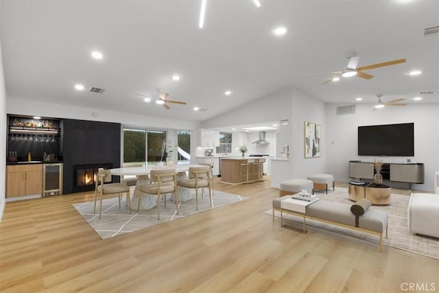 living room featuring lofted ceiling, beverage cooler, indoor bar, and light hardwood / wood-style flooring