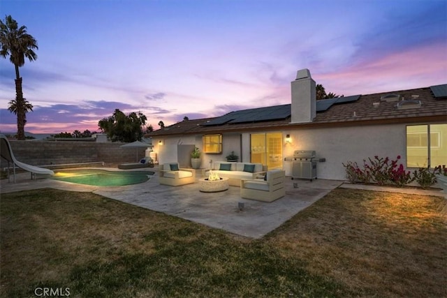 back house at dusk with a fire pit, a yard, a fenced in pool, a patio area, and solar panels