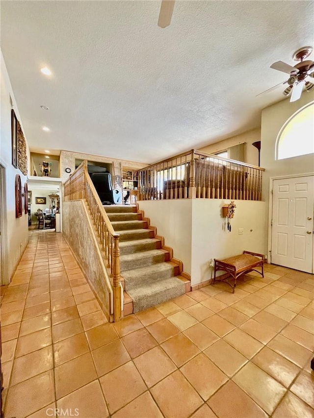 staircase featuring ceiling fan, lofted ceiling, tile patterned flooring, and a textured ceiling