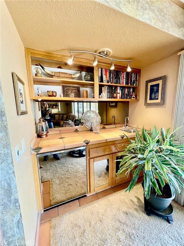 bar with sink, rail lighting, dishwasher, tile patterned flooring, and a textured ceiling