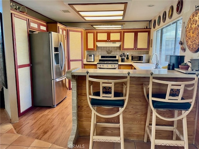 kitchen with appliances with stainless steel finishes, sink, backsplash, kitchen peninsula, and light hardwood / wood-style flooring