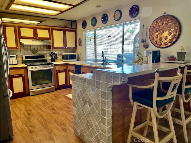 kitchen with appliances with stainless steel finishes, a kitchen breakfast bar, tasteful backsplash, kitchen peninsula, and light wood-type flooring