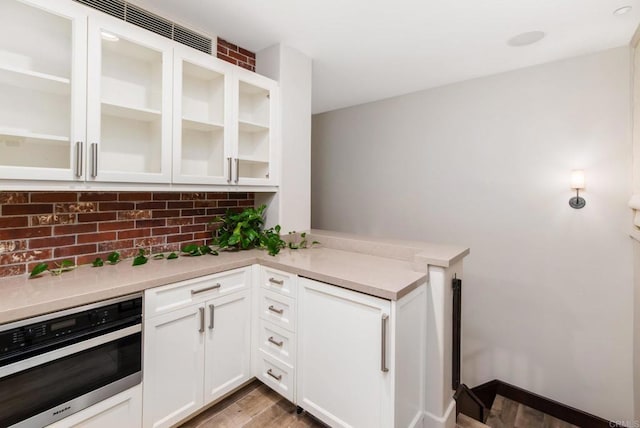 kitchen with decorative backsplash, light hardwood / wood-style flooring, stainless steel oven, and white cabinets