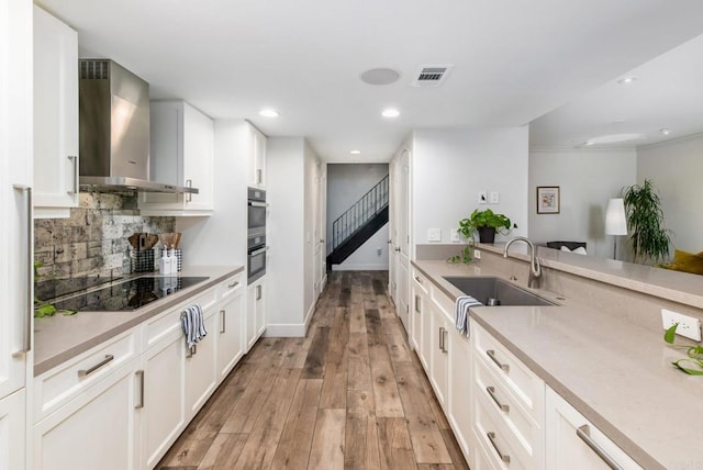 kitchen featuring sink, black electric stovetop, white cabinets, and wall chimney exhaust hood