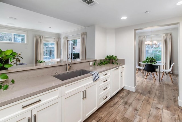 kitchen featuring sink, light hardwood / wood-style flooring, a wealth of natural light, white cabinets, and decorative light fixtures