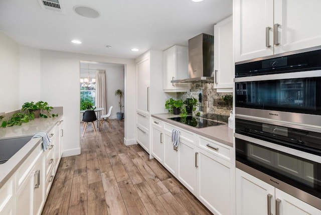 kitchen with wall chimney range hood, light wood-type flooring, black electric stovetop, decorative backsplash, and white cabinets