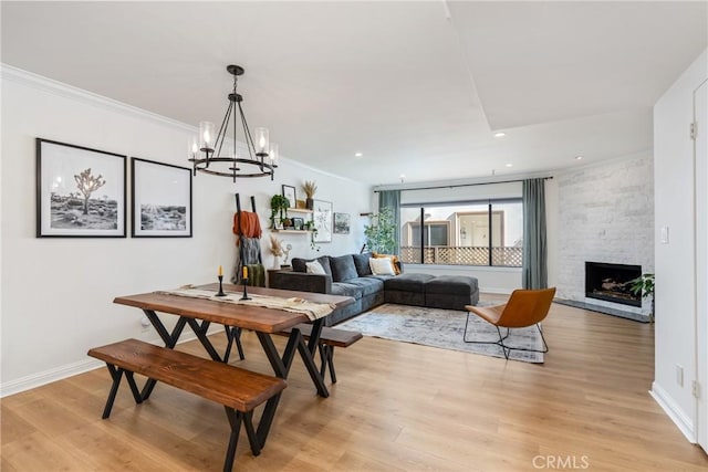 dining area featuring crown molding, a notable chandelier, a fireplace, and light wood-type flooring