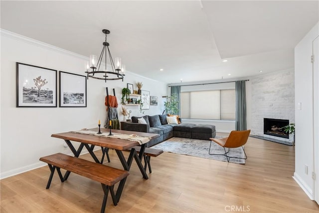 dining space with crown molding, a notable chandelier, a fireplace, and light hardwood / wood-style flooring