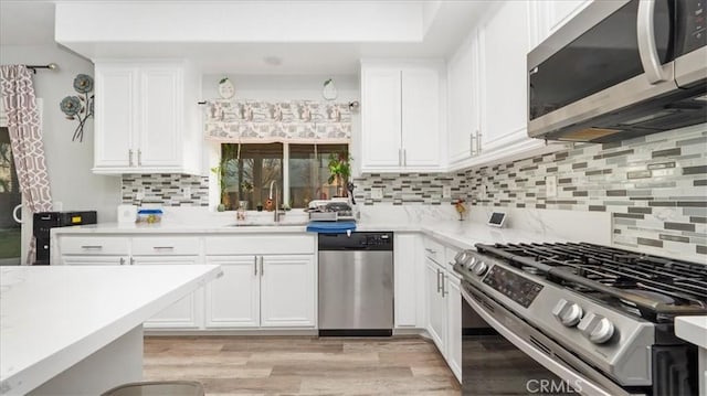 kitchen featuring sink, backsplash, stainless steel appliances, white cabinets, and light wood-type flooring