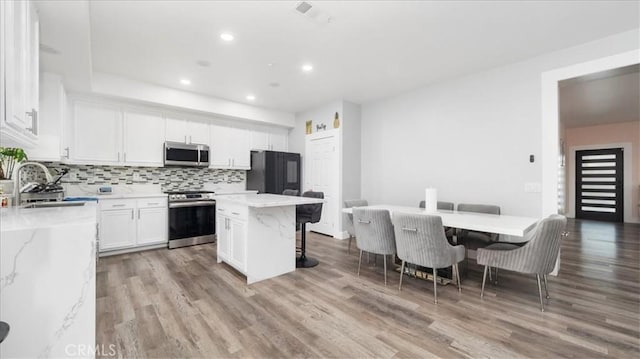 kitchen featuring a kitchen island, appliances with stainless steel finishes, white cabinetry, sink, and a kitchen bar